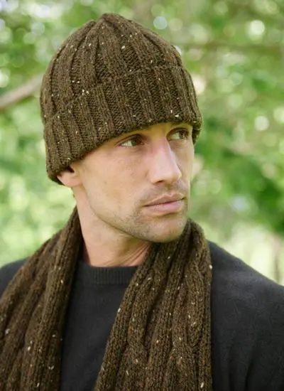 Close-up shot of man standing in grassy park wearing matching olive colored knit hat and scarf